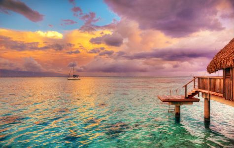 A serene seascape at sunset, featuring a wooden dock, a sailboat on calm waters, and a vibrant sky with colorful clouds.