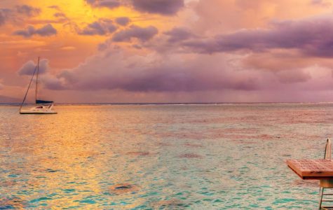 A serene seascape at sunset, featuring a wooden dock, a sailboat on calm waters, and a vibrant sky with colorful clouds.