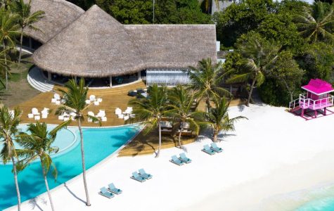 Aerial view of a resort featuring a sparkling pool and a sandy beach, surrounded by lush greenery.