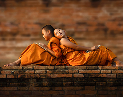 Cambodian children dressed in traditional orange clothes sitting on a brick wall