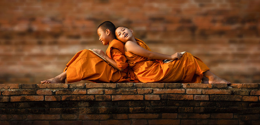 Cambodian children dressed in traditional orange clothes sitting on a brick wall