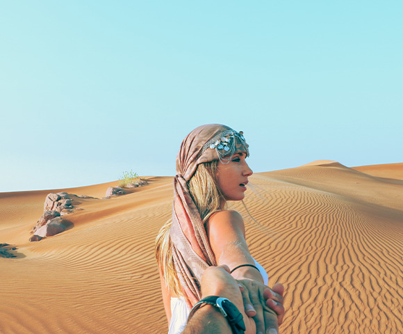 Lady with head scarf on holding photographers hand while walking through the desert