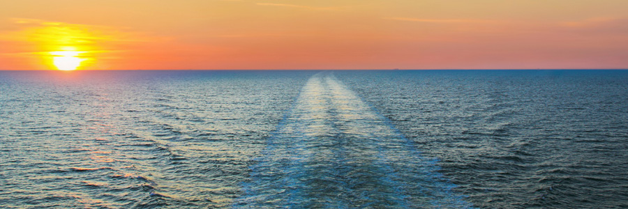 Sunset over a tranquil ocean, with gentle waves creating a foamy wake, casting a warm glow across the water.