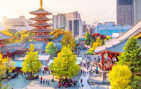 Vibrant autumn view of Tokyo’s Senso-ji Temple complex, with a red pagoda, ornate roofs, colorful trees, visitors, and skyline beyond.