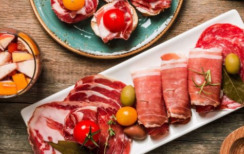 Rustic charcuterie spread with cured meats, olives and tomatoes on colorful plates over a wooden table.
