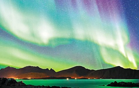 Vibrant auroras dance across a starry sky, illuminating the dark mountains and calm waters below in a spectacular display of colors.