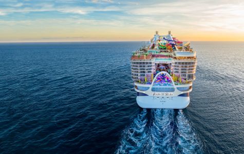 Royal Caribbean's Icon Class cruise ship, Icon of the Seas, viewed from behind, sailing toward a golden horizon with colourful attractions visible on deck.