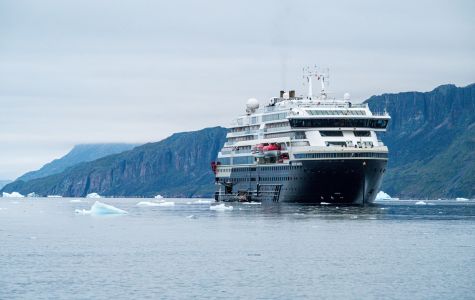 A large cruise ship sailing in the water, surrounded by mountains under a clear sky.