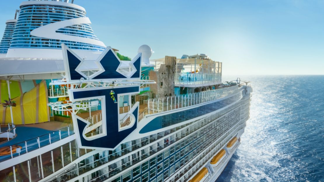 A Royal Caribbean cruise ship features a large logo and sunny decks overlooking the shimmering ocean.