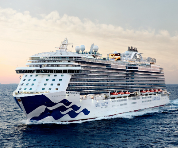 The Royal Princess cruise ship sails through calm waters, illuminated by a sunset skyline in the background.
