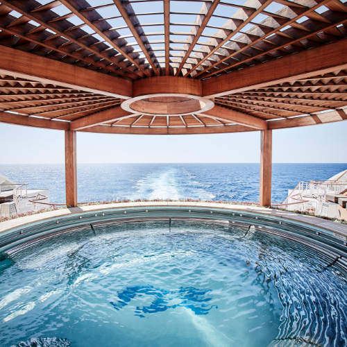 A luxurious hot tub under a wooden pergola overlooks a serene ocean view, creating a tranquil, inviting atmosphere.