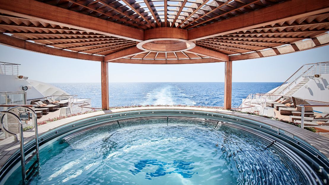 A luxurious hot tub under a wooden pergola overlooks a serene ocean view, creating a tranquil, inviting atmosphere.