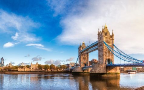 Panoramic view of Tower Bridge over the River Thames, with vibrant blue sky and reflections in the water, showcasing iconic London architecture.