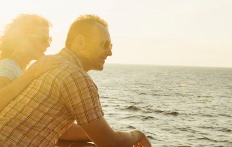 A couple enjoys a sunset together on a cruise ship, gazing at the ocean while leaning on the railing.