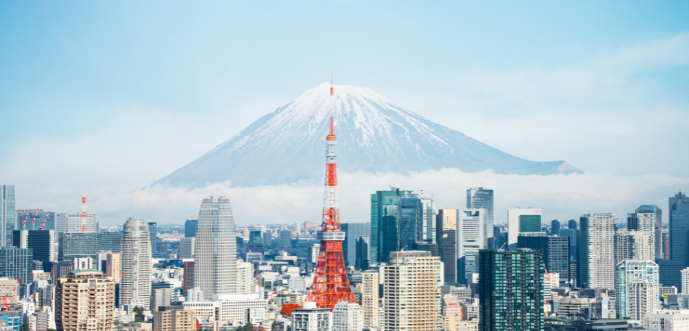Tokyo skyline featuring the iconic Tokyo Tower in foreground with Mount Fuji majestically rising in the background under a clear blue sky.