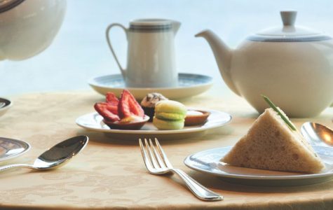 A beautifully arranged table with tea, assorted pastries, sandwiches, and cutlery, set against a window view.