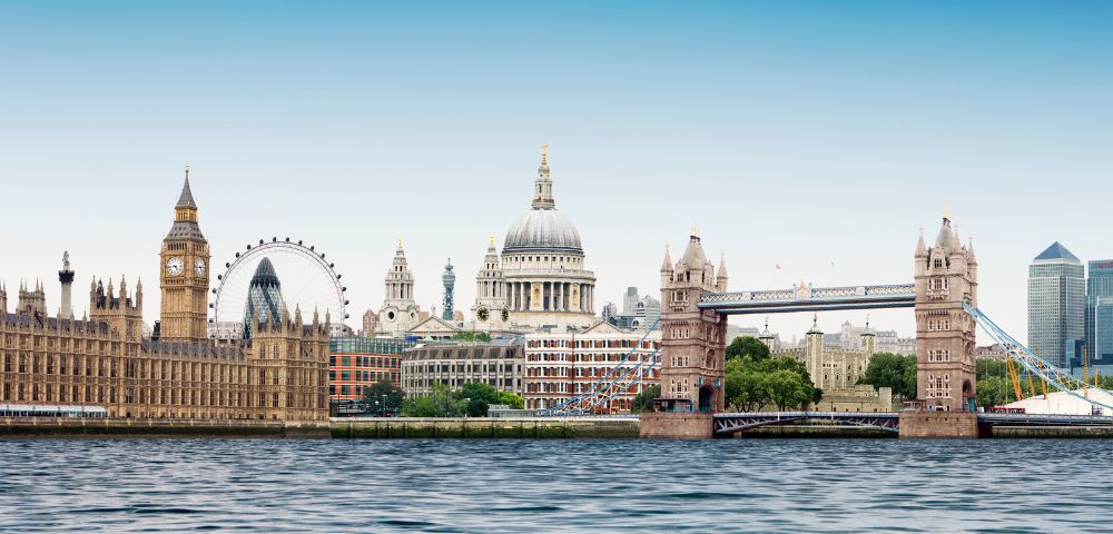 London skyline with landmarks including Big Ben, the London Eye, and Tower Bridge. The scene captures a clear day by the River Thames.