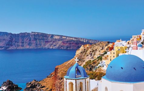 Scenic view of Santorini with white buildings and blue domes overlooking the Aegean Sea, with cliffs and a clear blue sky in the background.