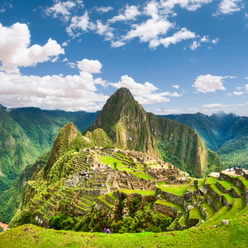 Ancient Incan ruins of Machu Picchu with terraced hillsides under a bright blue sky with scattered clouds.