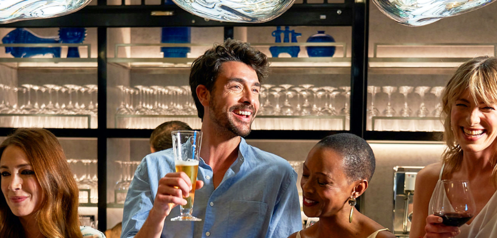 Group of four friends smiling and holding drinks while socializing in a modern bar setting.