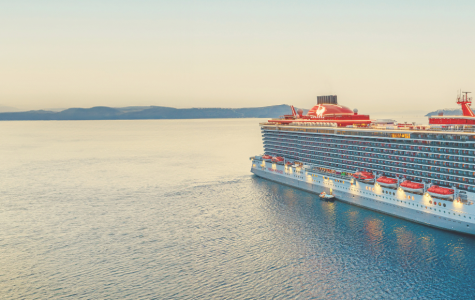 Large cruise ship sailing on calm sea near rocky cliffs under clear sky at sunset.