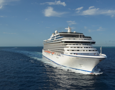 Large white cruise ship sailing through calm blue ocean under a partly cloudy sky.