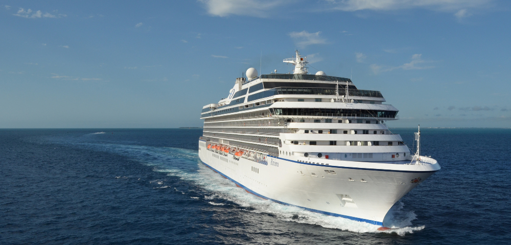 Large white cruise ship sailing through calm blue ocean under a partly cloudy sky.