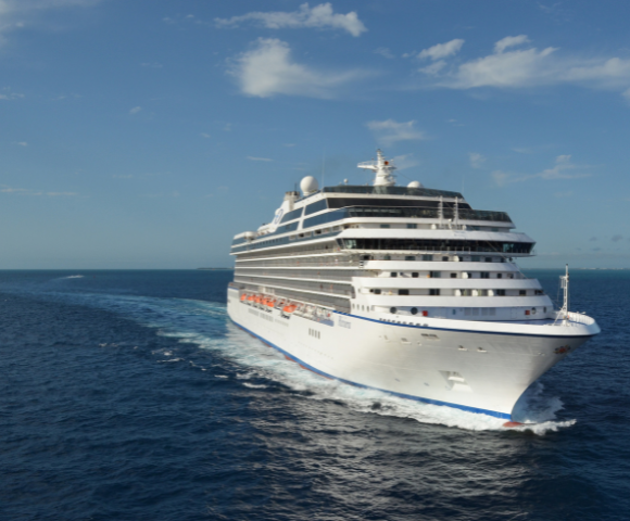 Large white cruise ship sailing through calm blue ocean under a partly cloudy sky.