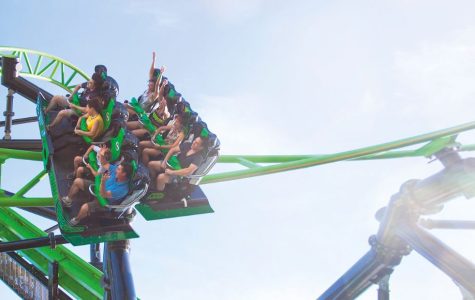 Thrilling roller coaster ride under a bright blue sky, with passengers holding on as the green and black track twists dynamically through the air.