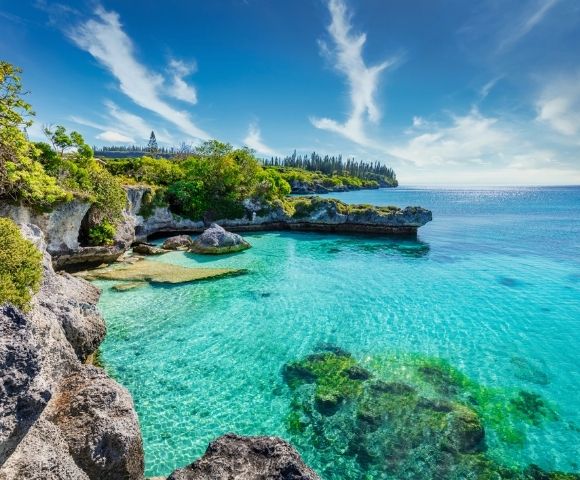 A tropical coastline with clear turquoise waters, rocky outcrops, and lush greenery under a blue sky.