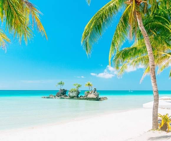White sand, palm tree lined beach with aqua water, blue sky and small island offshore