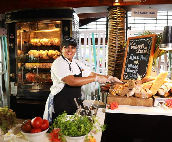 MYHOLIDAY-RADISSON-BLU-RESORT-FIJI-DENARU-ISLAND-WOMAN-BEHIND-COUNTER-CUTTING-BREAD-AND-SERVING-CHICKEN