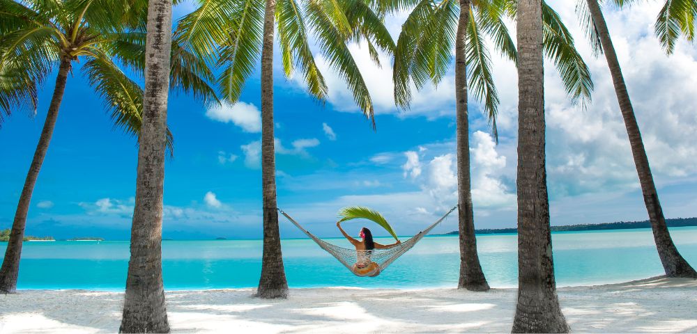 myholiday-woman-laying-in-a-hammock-looking-at-the-beach-and-crystal-clear-waters-of-Aitutaki-Lagoon-Private-Island-Resort