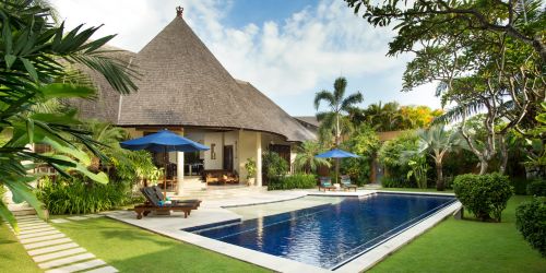 Scenic view of villa with pool, grass and deck chairs at The Kunja Villas & Spa in Bali