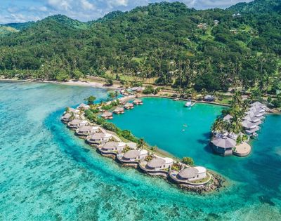 Aerial view of resort showing reef and over water villas with the lush jungle in the background