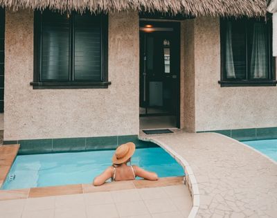 woman in hat enjoying private pool outside bure with small bridge and thatched roof