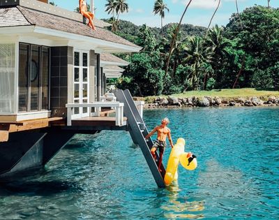 man climbing ladder to overwater bungalow holding inflatable duck
