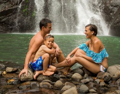 mother father and son sitting on the waters edge with a waterfall in the background