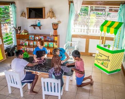 five children drawing on a blackboard table with a play lemonade stand in the background