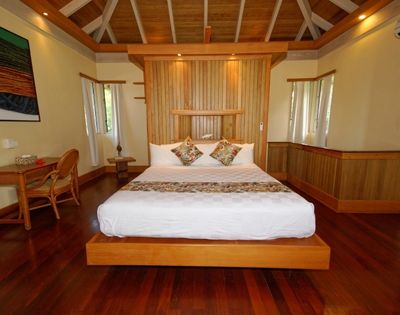 bed with white bedding and wooden framing with hard wood floor and desk with chair on left side