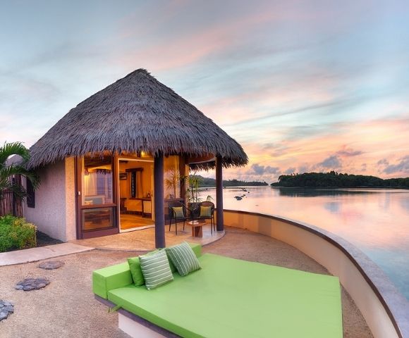 Green out door bed with villa in background and ocean views at sunrise