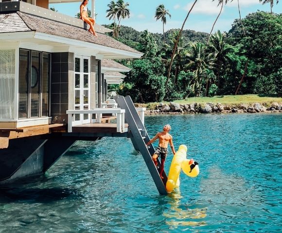 man climbing ladder to overwater bungalow holding inflatable duck