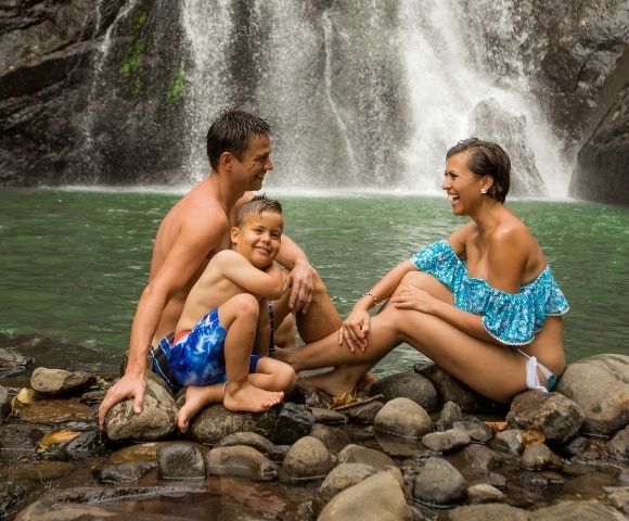 mother father and son sitting on the waters edge with a waterfall in the background