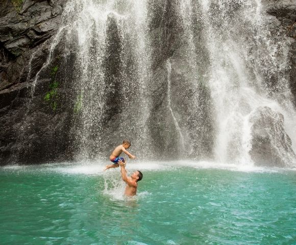 father throwing his son up in the air while playing in the water in front of a waterfall