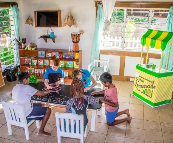 five children drawing on a blackboard table with a play lemonade stand in the background
