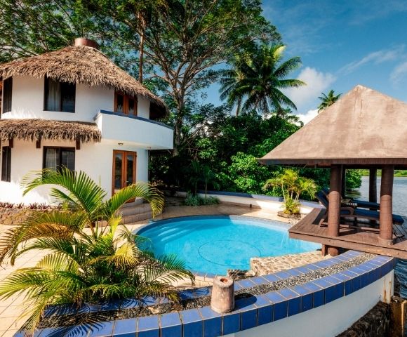 white two story villa with thatched roof and private pool and patio overlooking the water