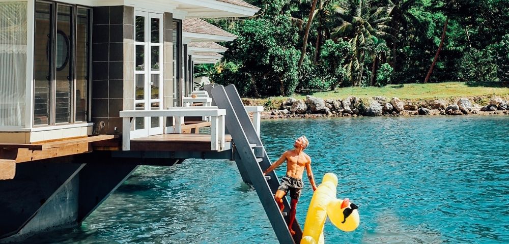 man climbing ladder to overwater bungalow holding inflatable duck