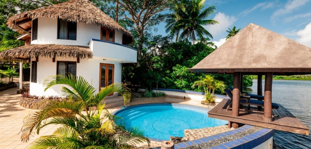 white two story villa with thatched roof and private pool and patio overlooking the water