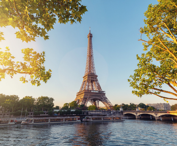 Eiffel Tower at sunset with Seine River and green foliage.