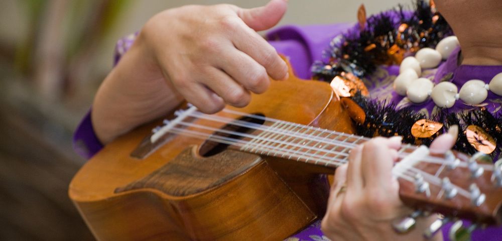 person in purple hawaiian shirt with two lei playing the ukulele